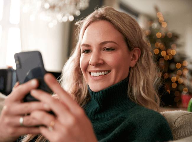 Close Up Of Woman Relaxing On Sofa At Home At Christmas Using Mobile Phone