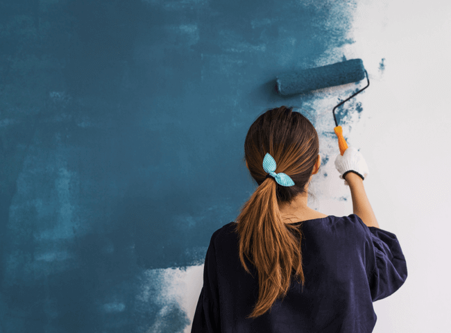 Happy woman painting interior wall with paint roller in new house