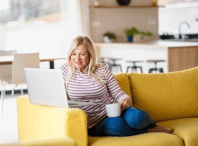 Senior woman with coffee and laptop indoors at home