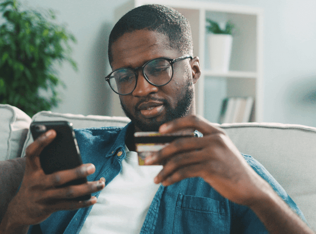young man in glasses shopping online with credit card using smart phone at home